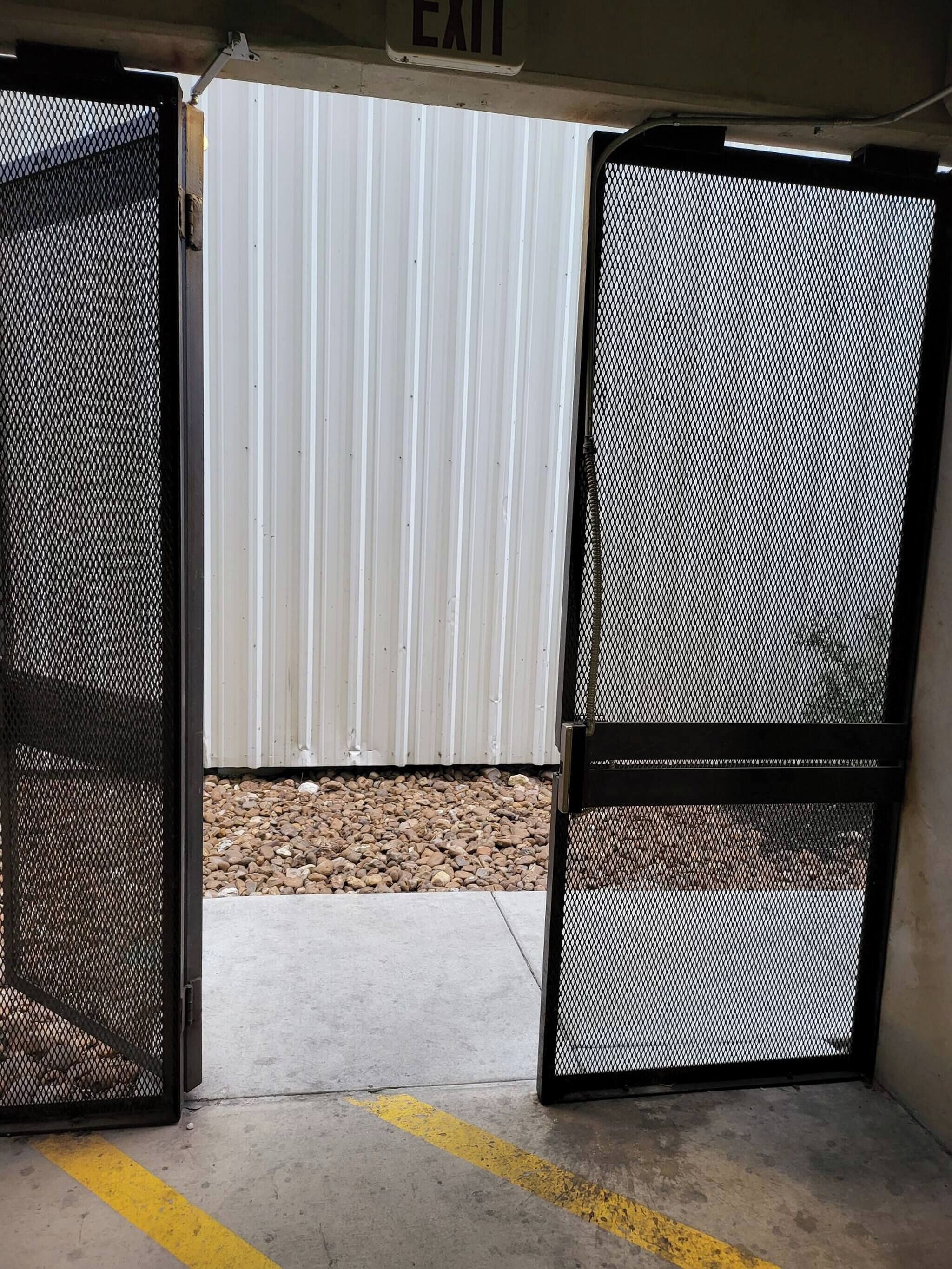 A metal gate with a mesh design, an EXIT sign above it, and a concrete floor with a yellow line.