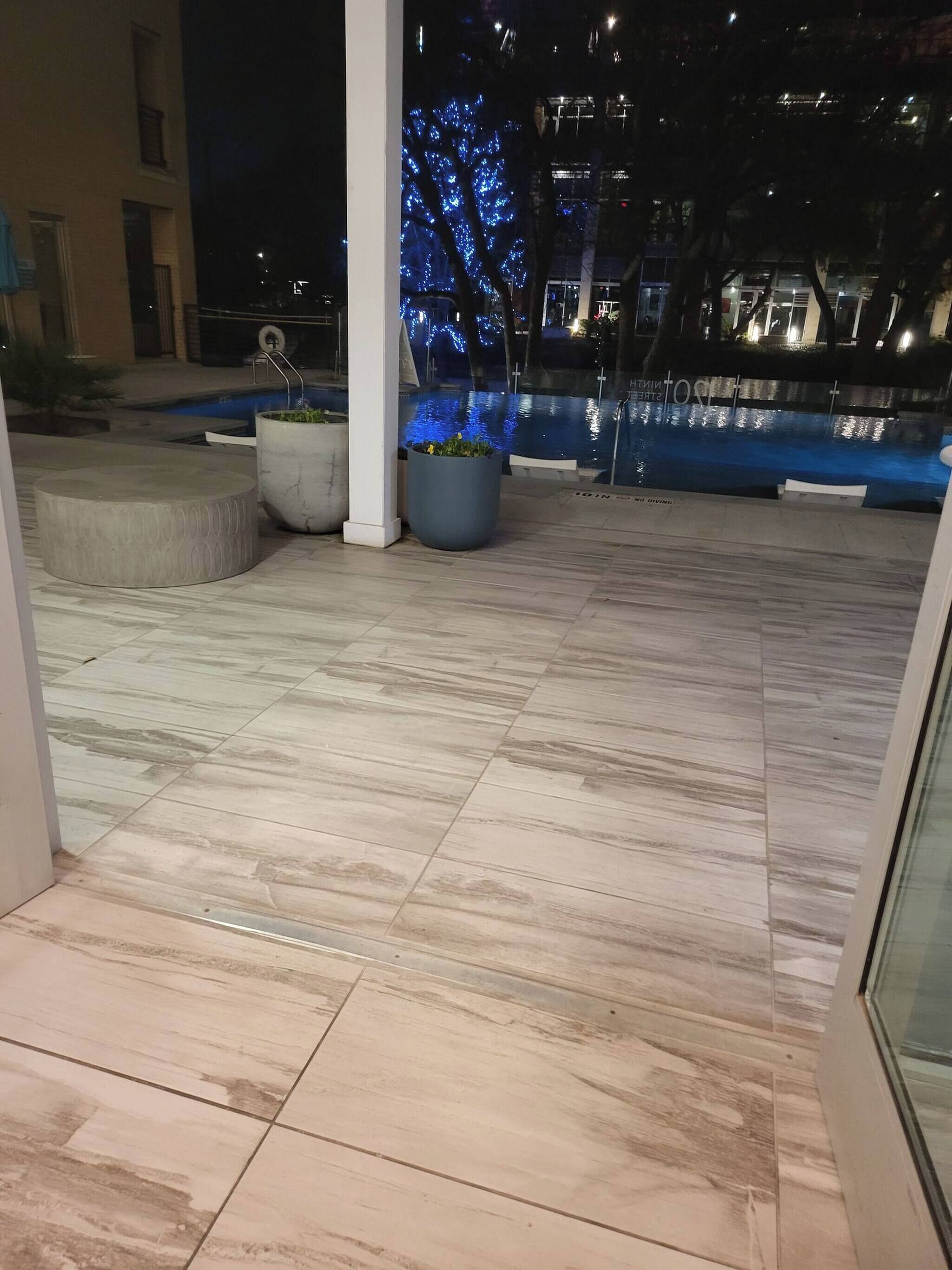 Ein Poolbereich mit gefliestem Boden, Pflanzkübeln und einem Pool mit blauer Beleuchtung.