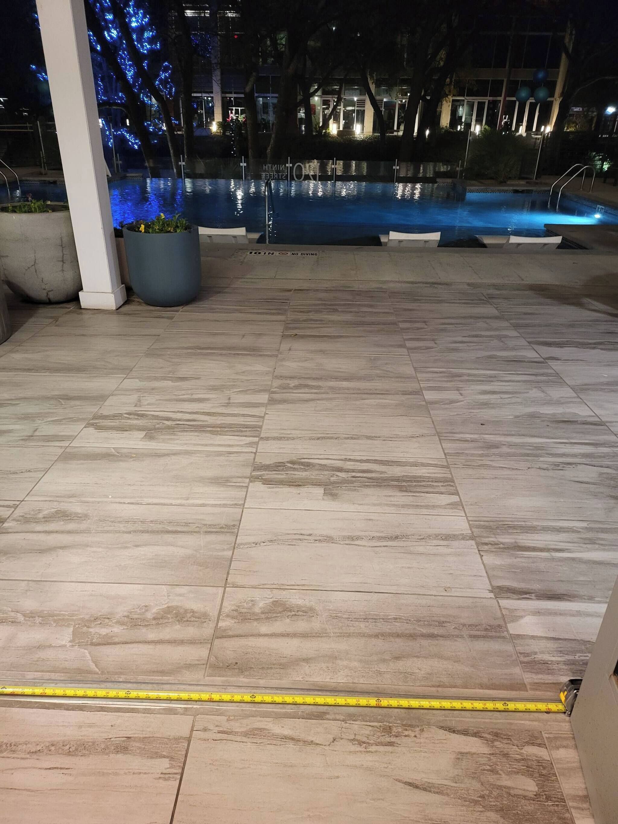 A poolside area with tiled flooring, potted plants, and a pool with blue lighting.