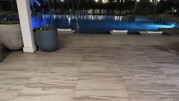 A poolside area with tiled flooring, potted plants, and a pool with blue lighting.