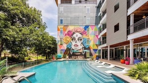 Uma piscina com um mural, uma placa de 1,2 metros proibindo saltos e um edifício com varandas.