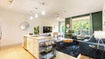 Een moderne woonkamer met een bank, salontafel en televisie. Er is een keukenhoek met een spoelbak en kastjes.