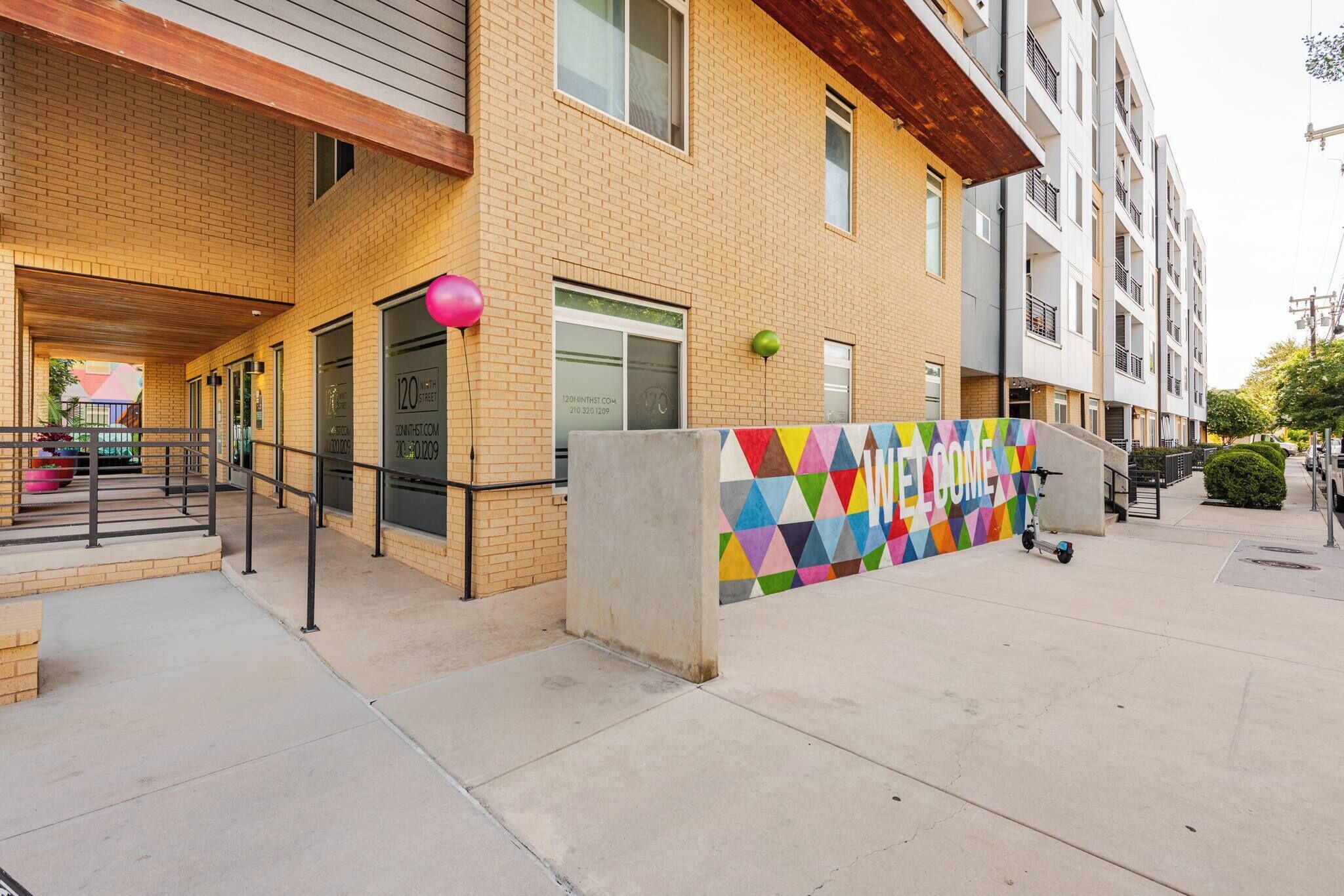 Un immeuble à plusieurs étages avec une façade en briques, un mur aux motifs géométriques colorés et un scooter garé à l’extérieur.