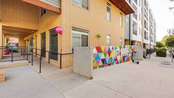 Un immeuble à plusieurs étages avec une façade en briques, un mur aux motifs géométriques colorés et un scooter garé à l’extérieur.