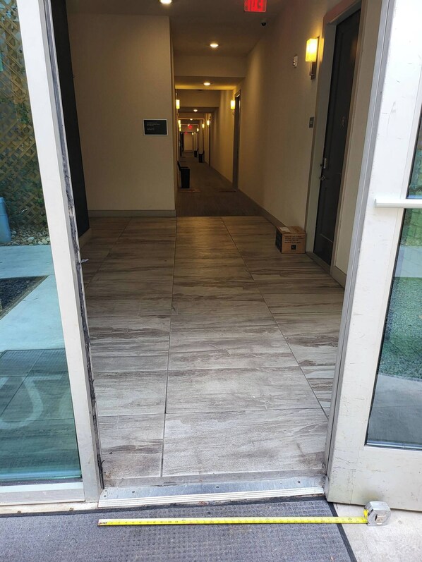 A hotel entrance with a tiled floor, a measuring tape, and a door leading to a corridor.
