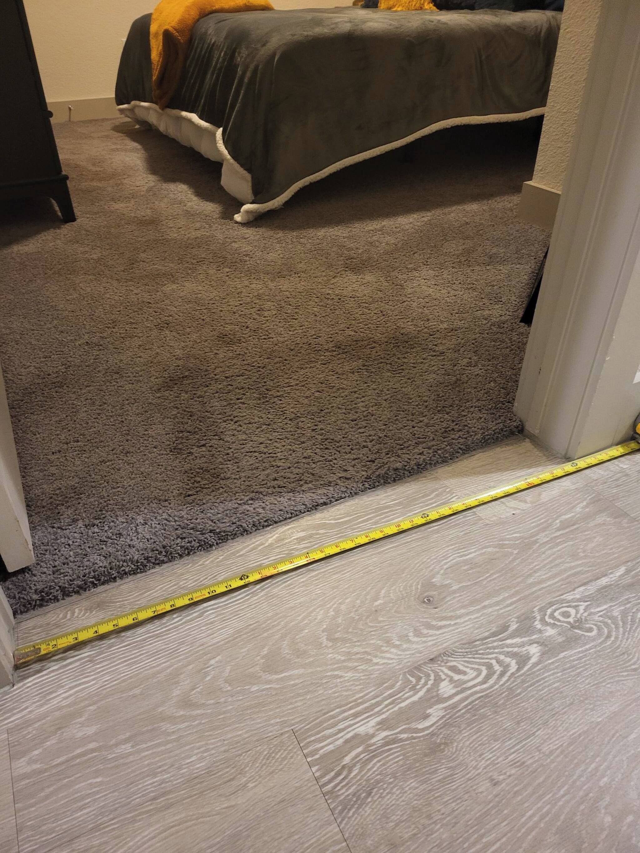 A carpeted hallway leading to a bedroom with a bed and a nightstand.