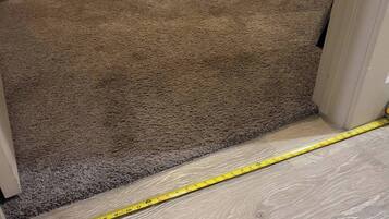 A carpeted hallway leading to a bedroom with a bed and a nightstand.
