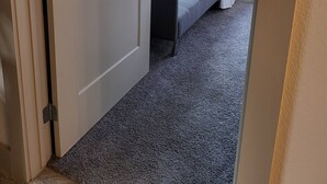 Um quarto com uma cama, um sofá cinzento, uma janela e uma porta.