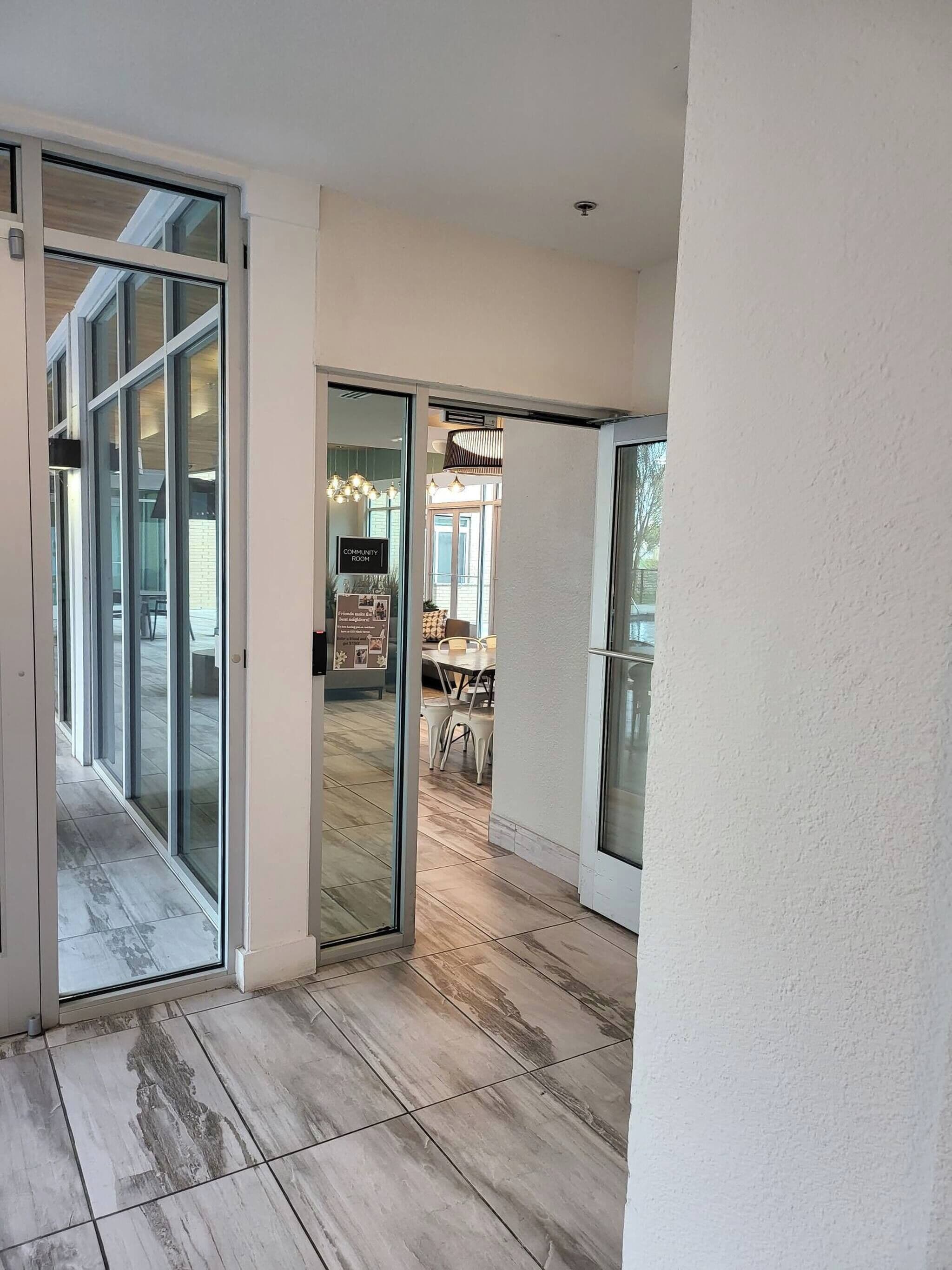 Un intérieur moderne avec une porte vitrée donnant sur un espace repas, un panneau indiquant l’accès à une salle commune et un ventilateur de plafond.