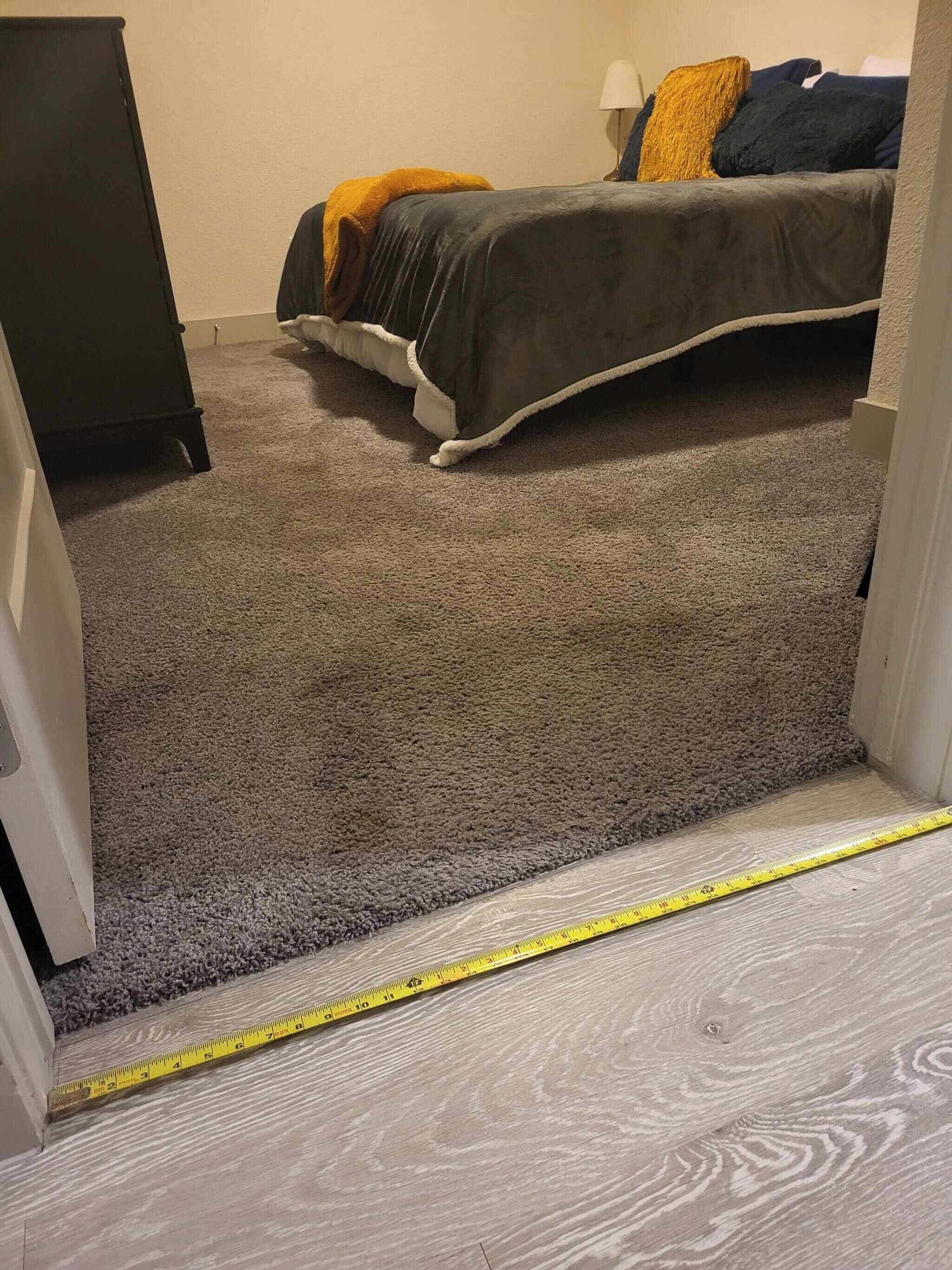 A carpeted room with a bed, a dresser, and a measuring tape on the floor.