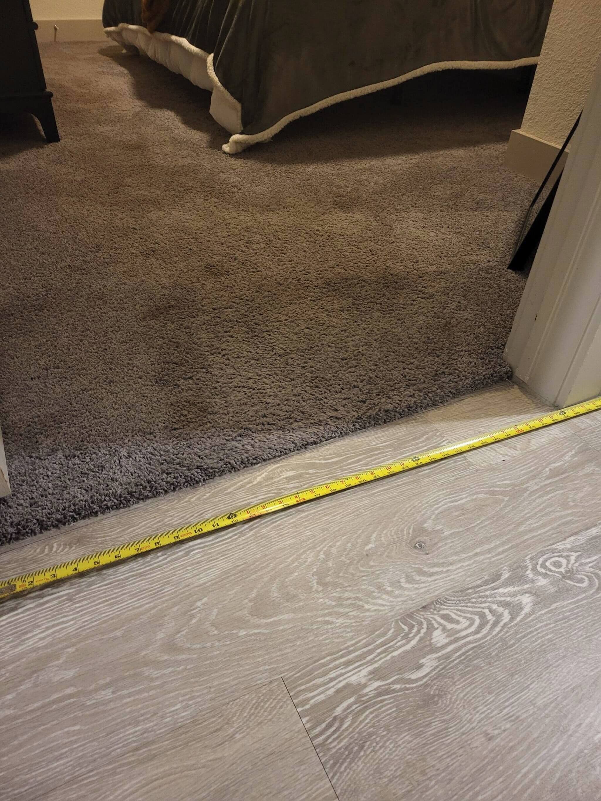 Een bekleed vloeroppervlak dat overgaat in een houten vloer, met een meetlint.