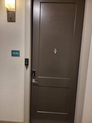 A closed door with a keypad lock, a doorbell, and a small emblem above the door. A number sign is visible on the wall to the left. - Chic Riverwalk Facing Condo Pool View Free Parking Pets Welcome (San Antonio)
