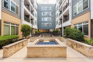 A multi-story residential building with balconies, a central courtyard with a water feature, and surrounding greenery. - Chic Riverwalk Facing Condo Pool View Free Parking Pets Welcome (San Antonio)