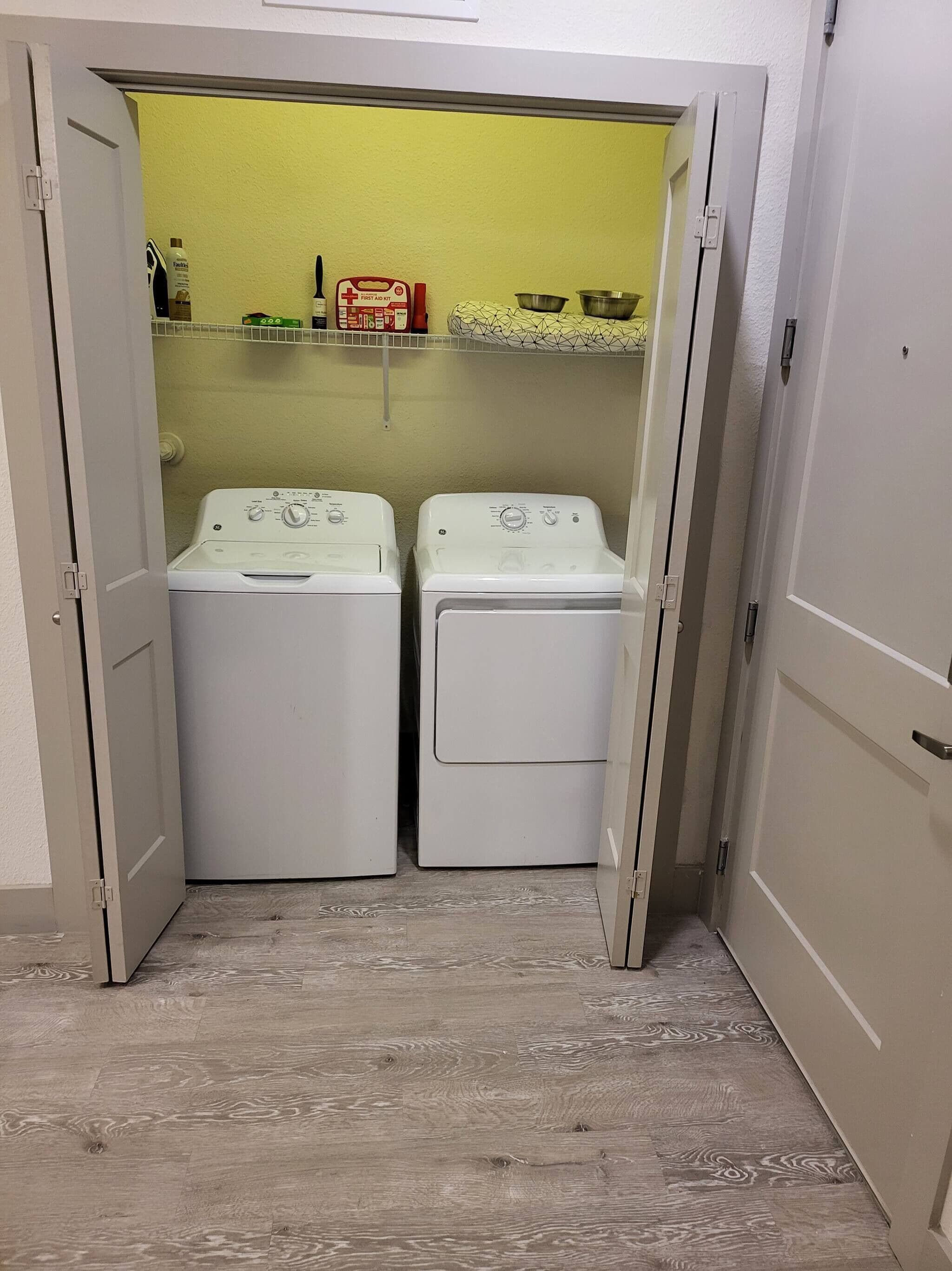 Una bugaderia amb dues rentadores blanques i una estant amb diferents objectes.
