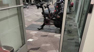 A gym area with exercise equipment, a trash bin, and a carpeted floor.