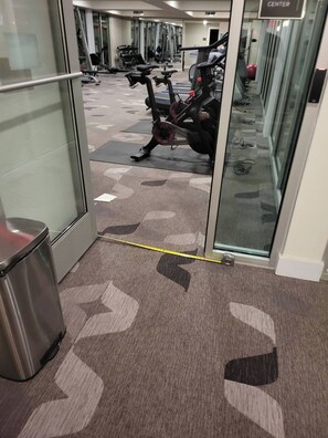 A gym area with exercise equipment, a trash bin, and a carpeted floor.