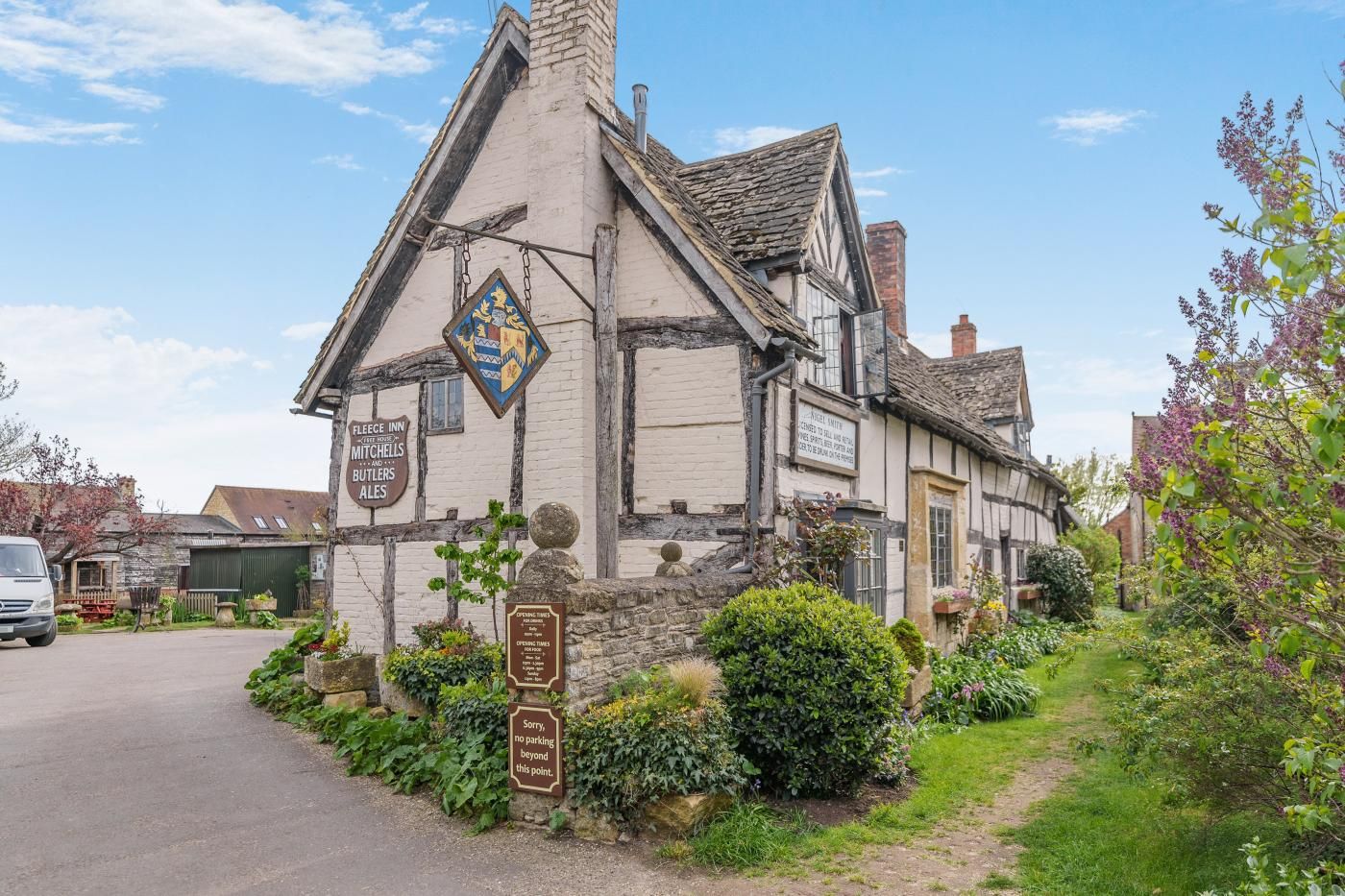 A traditional half-timbered building with a signboard indicating it is a pub, surrounded by greenery and a clear sky.