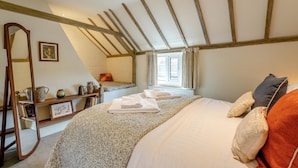 Ein Schlafzimmer mit schrägen Wänden, einem Bett mit ordentlich gefalteten Handtüchern, einem Nachttisch mit Dekoration und einem Fenster mit Vorhängen.