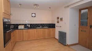 A kitchen with wooden cabinets, a black countertop, a clock, and a radiator. - 3 Bed in Wells (oc-55232) (Green Ore)