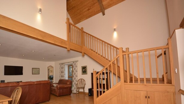A spacious living area with a wooden staircase, a leather sofa, a dining table, and a bookshelf. - 3 Bed in Wells (oc-55232) (Green Ore)