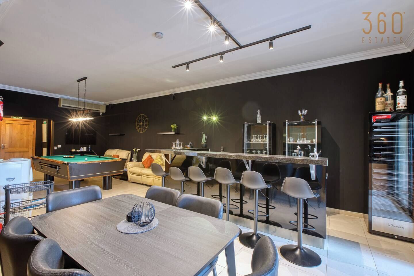 Zona de bar moderna con taburetes, mesa de billar y mostrador.