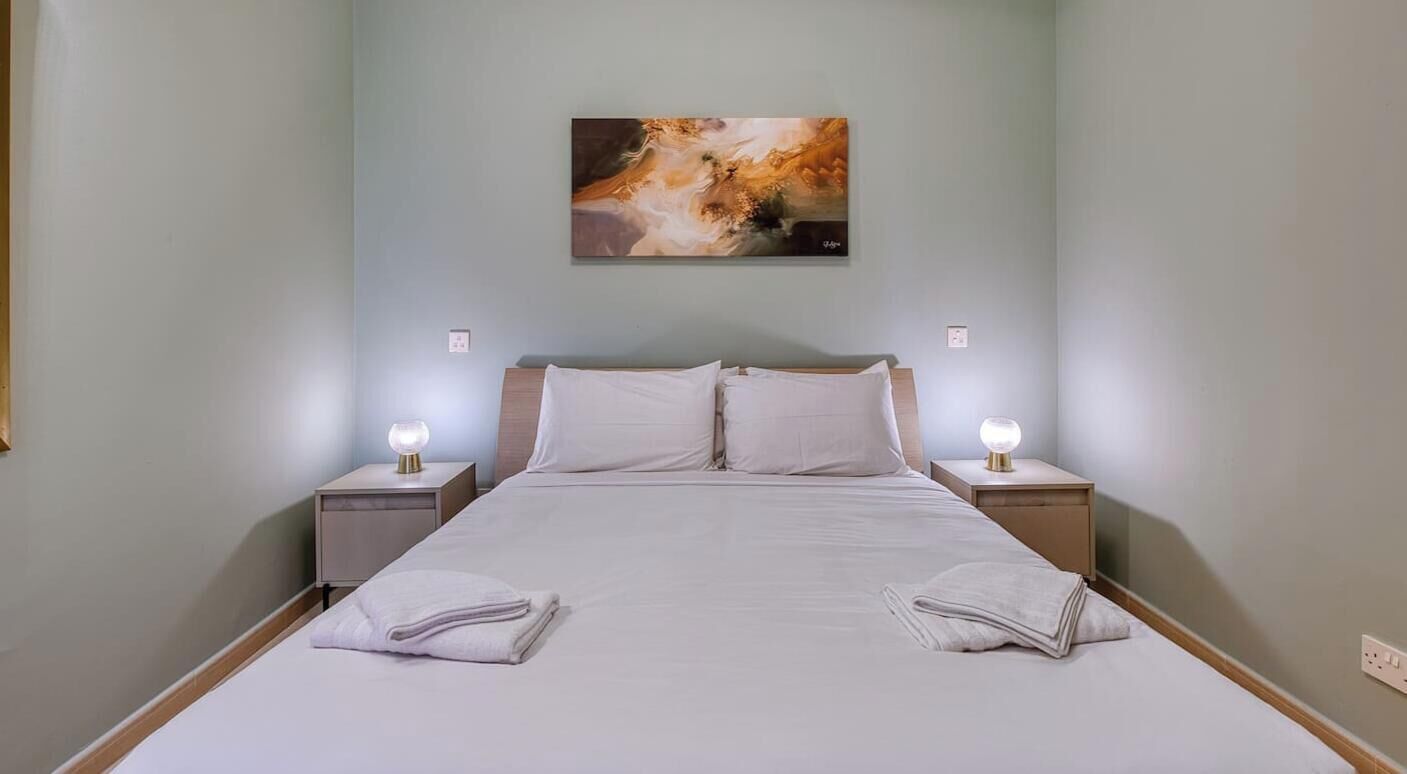 Une chambre d’hôtel avec un lit, deux tables de chevet avec des lampes et un tableau au mur.