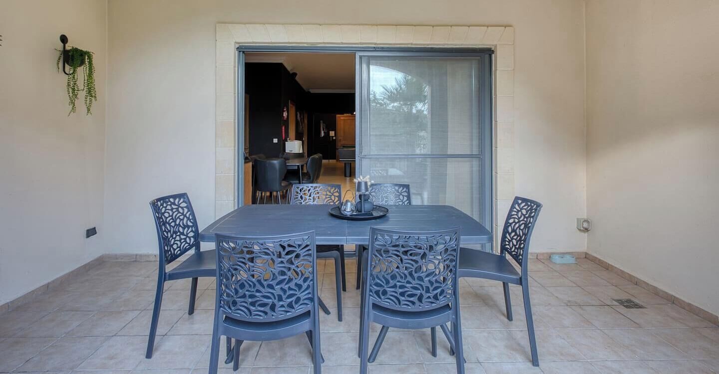 Comedor con mesa y sillas, una ventana y una puerta que da a otra habitación.