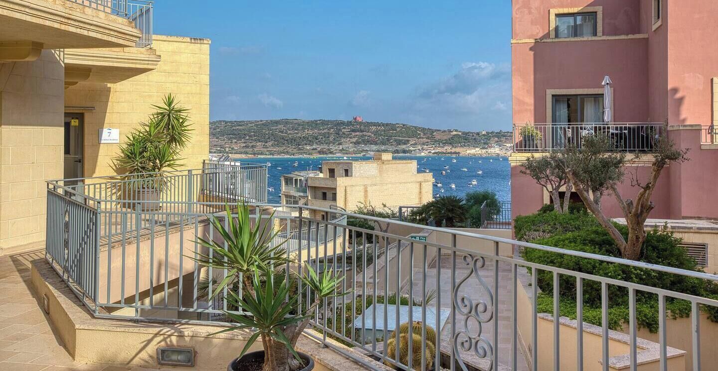 Un balcón con vista al mar, una planta en maceta y un edificio con balcón.