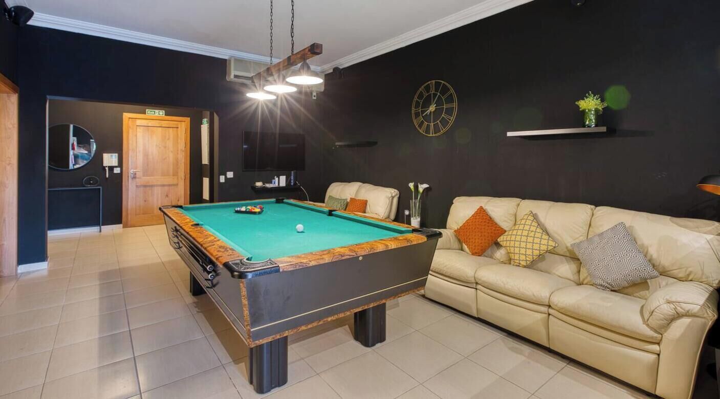 Una mesa de billar en una habitación con un sofá y un reloj en la pared.