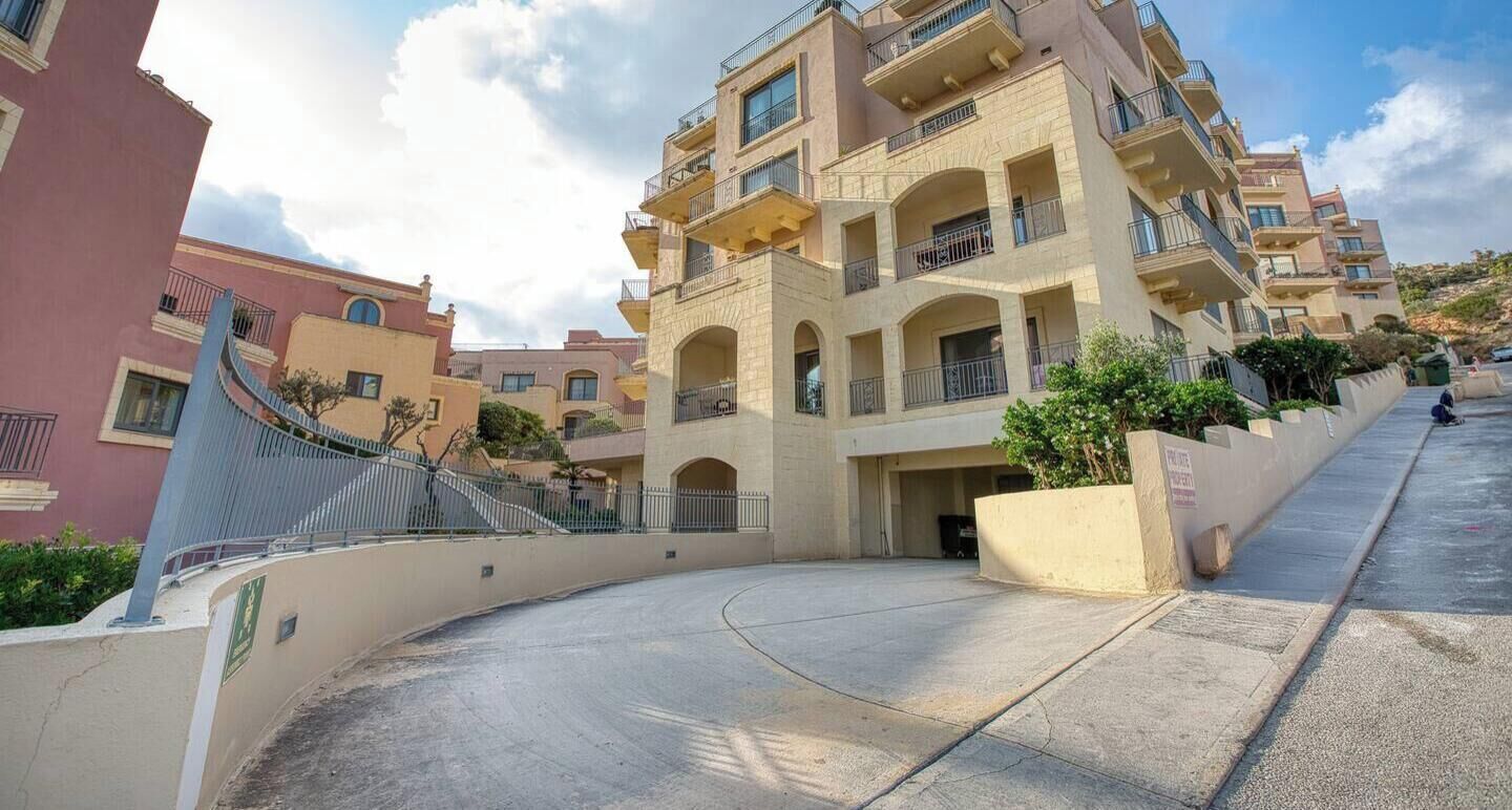 A multi-story residential building with balconies, a curved driveway, and a clear sky.