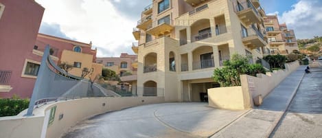 A multi-story residential building with balconies, a curved driveway, and a clear sky.