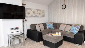 A living room with a sectional sofa, a coffee table, a flat-screen TV, and a clock on the wall. - 2 Bed in Pevensey (oc-55355) (Pevensey Bay)