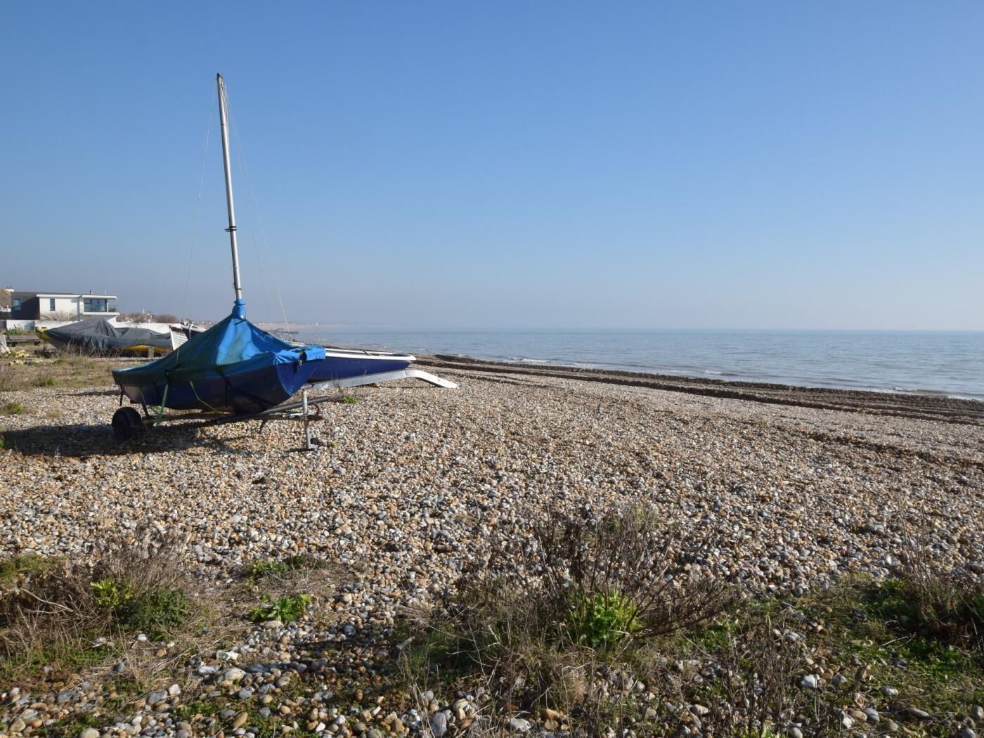 Una playa de guijarros con un velero y un toldo azul.