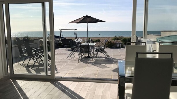A balcony with a table, chairs, and an umbrella overlooking a beach. - 2 Bed in Pevensey (oc-55355) (Pevensey Bay)