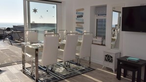 A dining area with a glass table, white chairs, a black rug, and a TV on the wall. - 2 Bed in Pevensey (oc-55355) (Pevensey Bay)