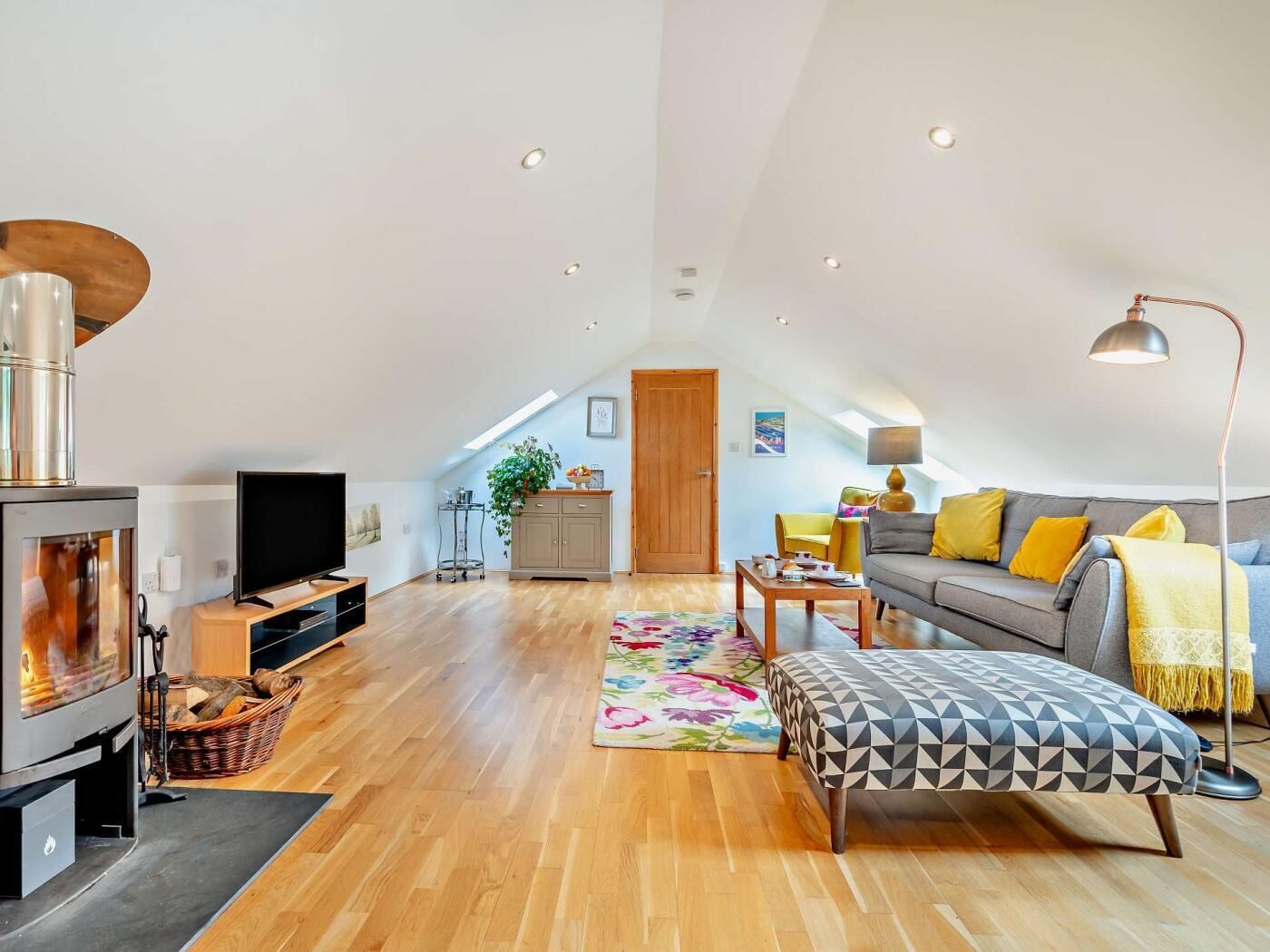 A spacious loft with a high ceiling, a fireplace, a sofa, a dining table, and a TV.