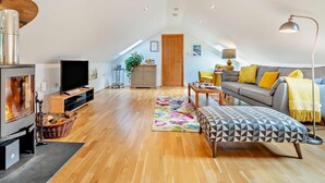 A spacious loft with a high ceiling, a fireplace, a sofa, a dining table, and a TV. - 1 Bed in Newquay (oc-55333) (Trebudannon)