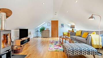 A spacious loft with a high ceiling, a fireplace, a sofa, a dining table, and a TV.