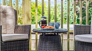 A balcony with wicker chairs and a table, a coffee pot, and a plate of strawberries.