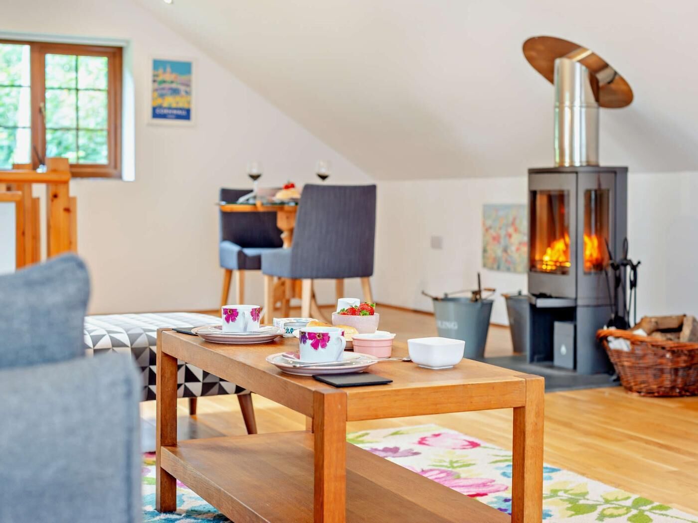 A cozy living room with a wooden table set for tea, a fireplace, and a dining area with chairs.