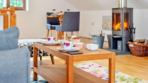 A cozy living room with a wooden table set for tea, a fireplace, and a dining area with chairs. - 1 Bed in Newquay (oc-55333) (Trebudannon)
