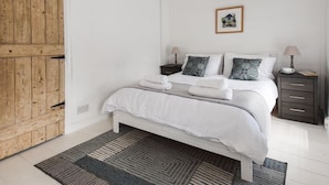 A bedroom with a wooden door, a bed with white bedding, two bedside tables with lamps, and a framed picture on the wall. - 3 Bed in Pwllheli (oc-55571) (Nefyn)