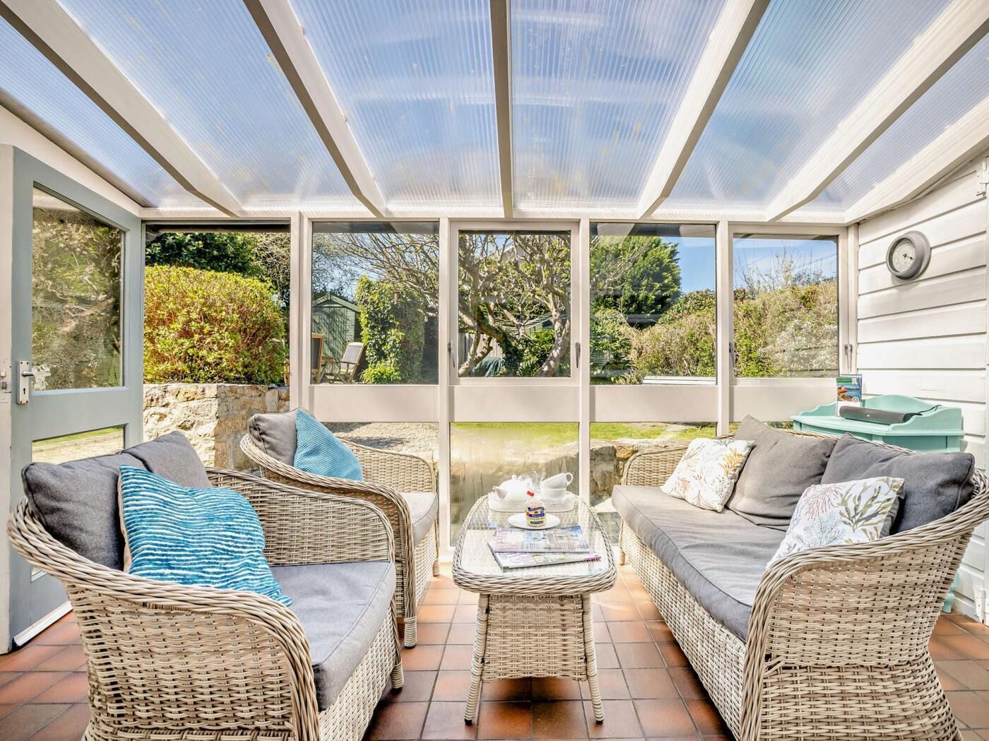 Un solárium con mobiliario de mimbre, techo de cristal y vistas al jardín.
