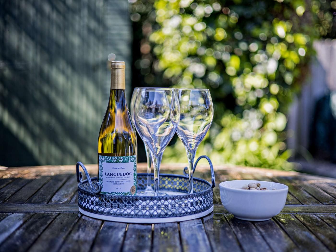 A bottle of wine, two glasses, and a bowl on a wooden table with a blue decorative tray.