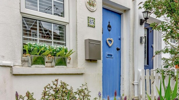 A white building with a blue door, a window with plants, and a white picket fence. - 1 Bed in Eastbourne (oc-ehc45) (Eastbourne)