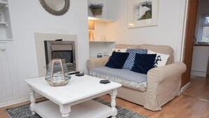A living room with a white coffee table, a beige sofa with patterned cushions, a fireplace, and a framed picture on the wall. - 1 Bed in Eastbourne (oc-ehc45) (Eastbourne)