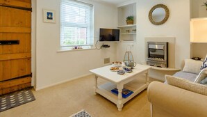 A living room with a fireplace, a television, a coffee table with pastries, and a sofa. - 1 Bed in Eastbourne (oc-ehc45) (Eastbourne)