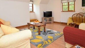A living room with a sofa, a coffee table with fruit, a TV on a cabinet, and a window with a view of trees. - 2 Bed in Canterbury (oc-55811) (Waltham)