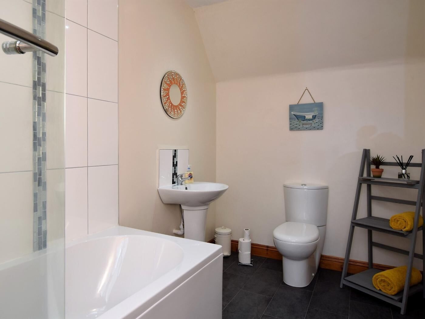 A bathroom with a bathtub, sink, toilet, and a shelf with towels.
