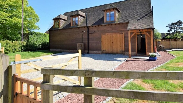 A wooden building with a garage, a gravel driveway, and a wooden fence. - 2 Bed in Canterbury (oc-55811) (Waltham)